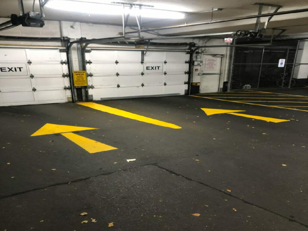 An Underground parking area of a condo apartment featuring paintings of sign arrows and exit signs on the garage door by Desa Contracting, Restoration, and Janitorial Services