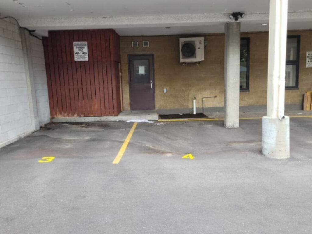 Displaying a parking space painted by Desa Contracting, Restoration, and Janitorial Services underneath a condo apartment in Toronto with two pillers and parking lights.