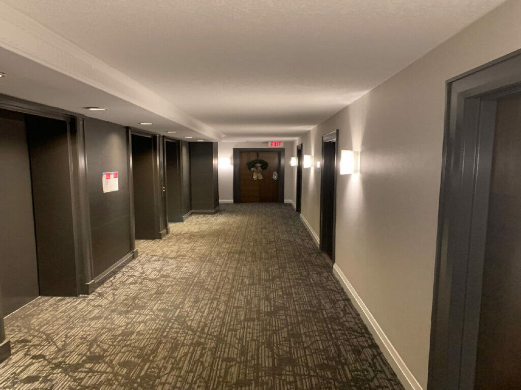 The restored corridor of Desa Contracting, Restoration, and Janitorial Services is visible, as are three recently renovated doors on the left, an escape sign, and lights above it.