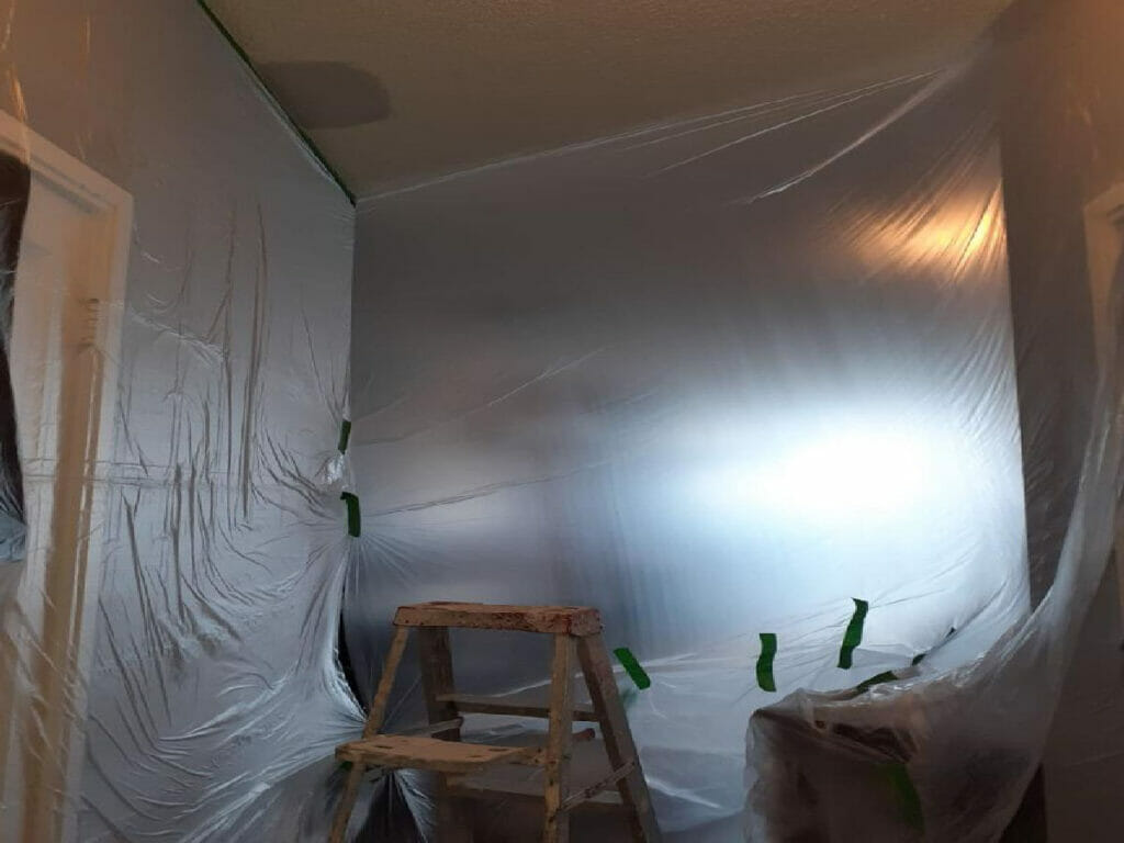 Desa Contracting, Restoration, and Janitorial Services is working on WATER DAMAGE RESTORATION in a space that is coated in polyethylene films and has a ladder in it.