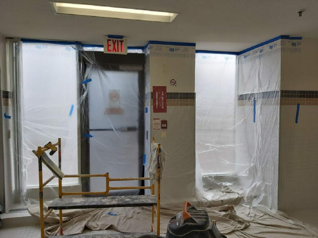 Desa Contracting, Restoration, and Janitorial Services Experts demonstrating a room wrapped with polyethylene and equipped with an exit sign at the top while working on water damage restoration.