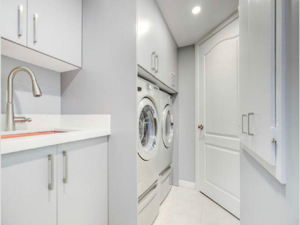 Desa Contracting and Restoration presents the renovated laundry room of a Toronto home, showcasing a washer and dryer, cabinets both on top and bottom, and a spacious doo