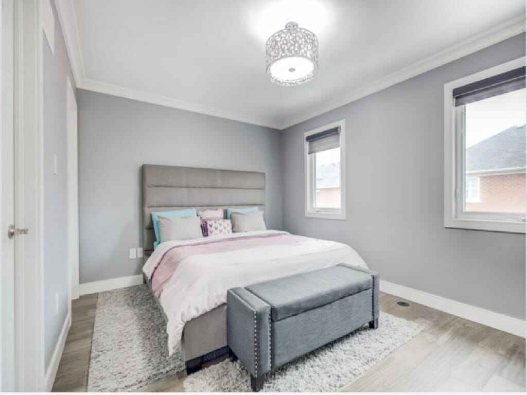 Desa Contracting and Restoration's Toronto bedroom remodel features a queen size bed, carpet, two windows, and a single ceiling chandelier.