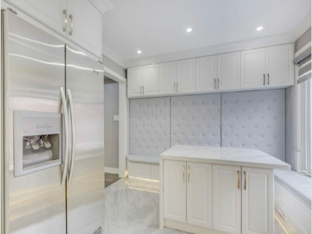 Desa Contracting and Restoration's Toronto kitchen remodel boasts the integration of pot lights, cabinets, a generous refrigerator, a central fruit table, as well as additional cabinets and a seating area adorned with cushioned walls.