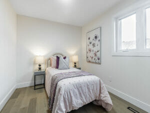 Desa Contracting and Restoration have transformed a Toronto home, showcasing a cozy bed with two lamps placed next to each other, complemented by a wall painting and a window, creating a comfortable and inviting space.