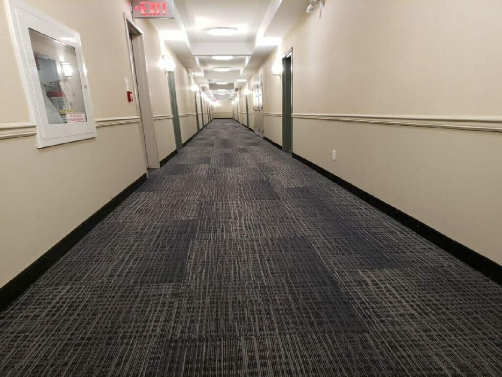 Displaying the hallway renovation work done by Desa Contracting, Restoration, and Janitorial Services, which includes doors on both sides and ceiling lights.