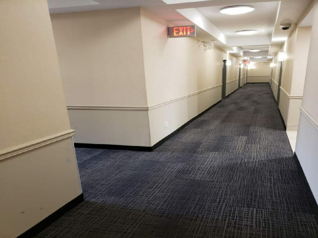 After renovation by Desa Contracting, Restoration, and Janitorial Services, it has a long, spotless hallway with ceiling lights and exit sign on the left.